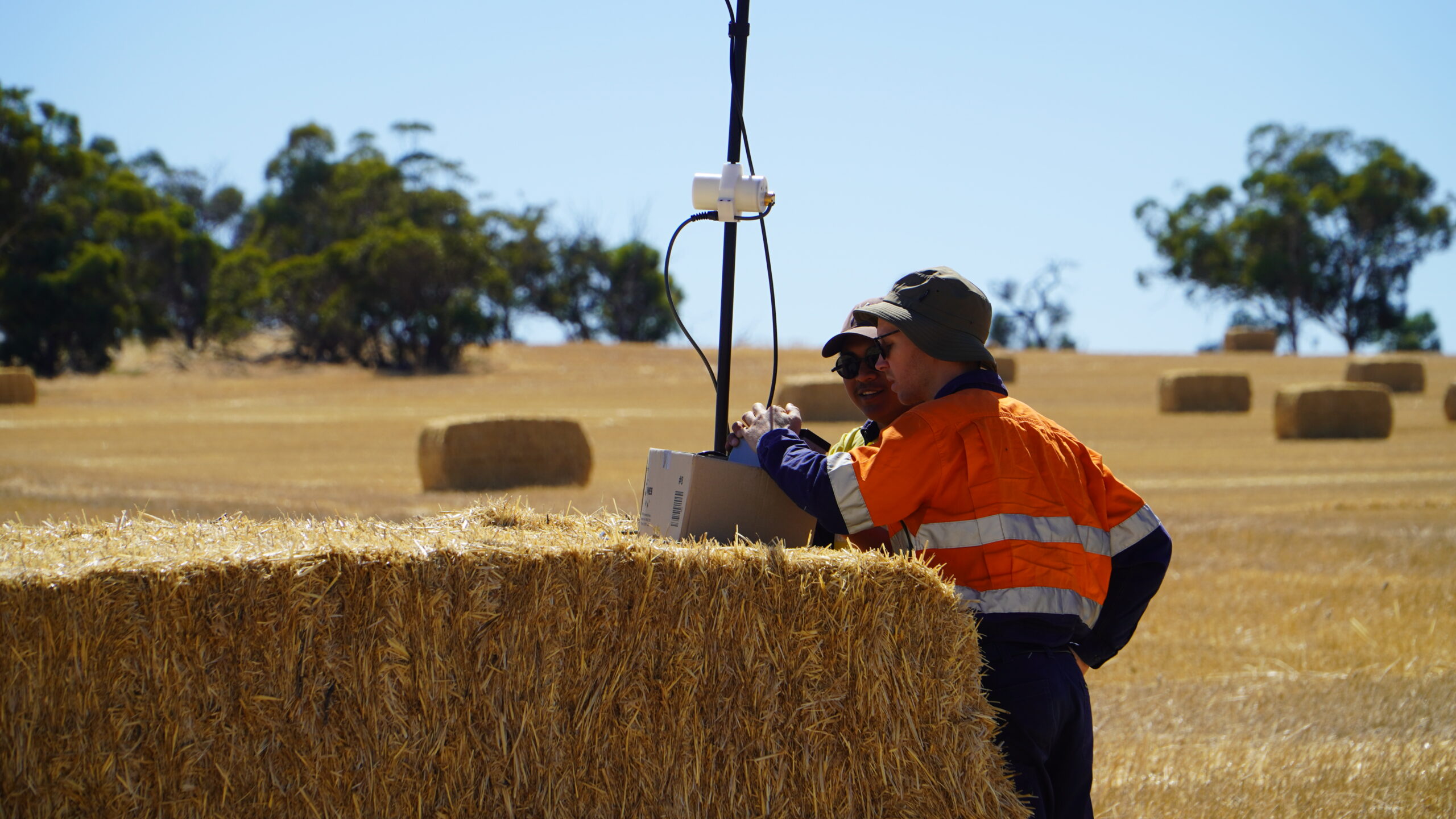 Two people looking at drone equipment on top of a hay bale.