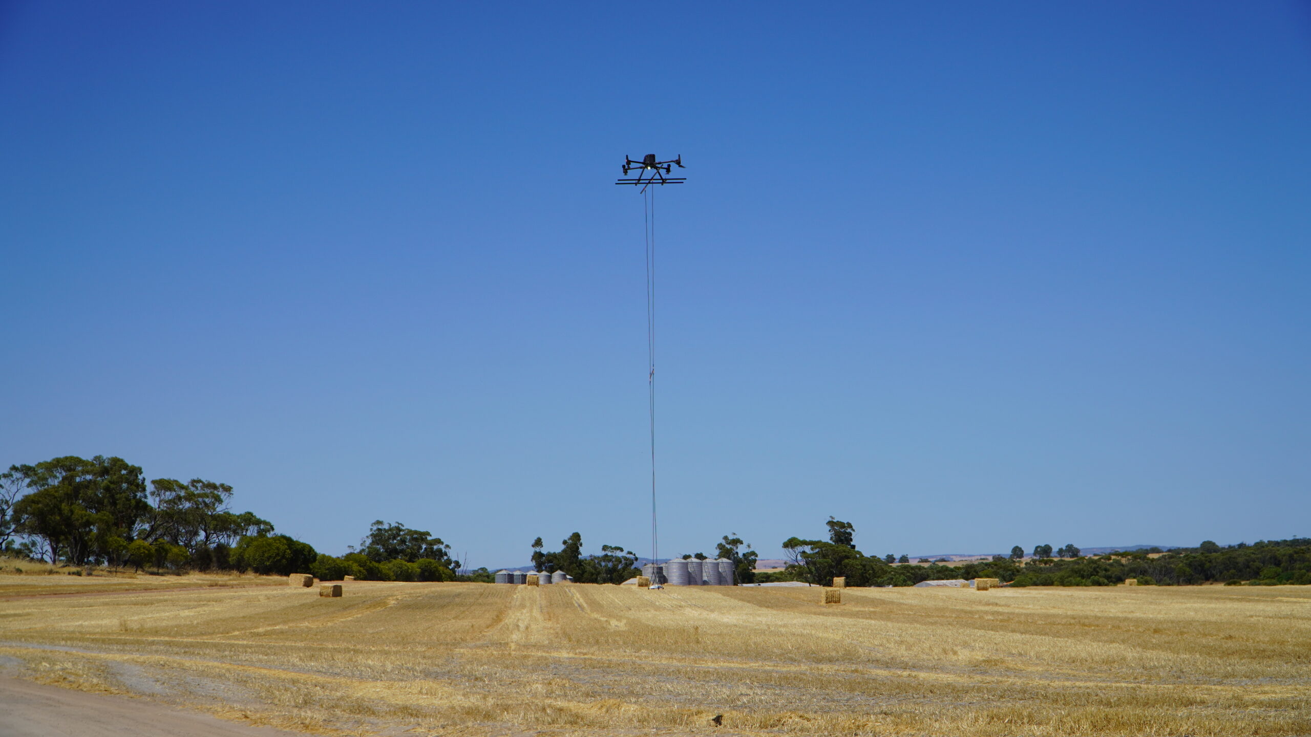Sensorem drone performing a magnetometer survey across farmland with water tanks in the background.